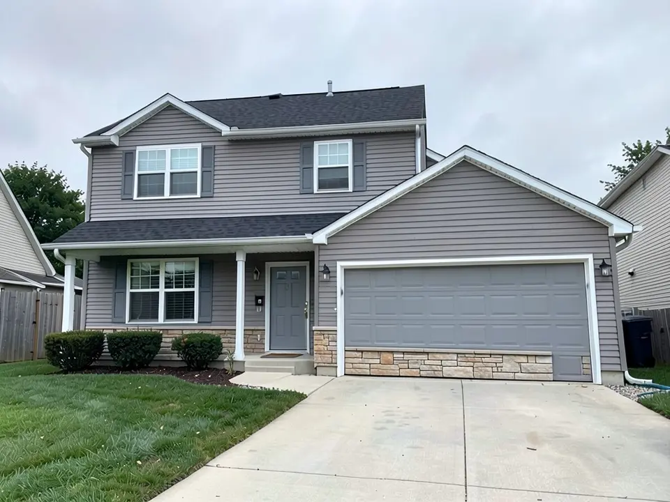 The same house with a band of natural stone veneer along the base of the garage wall and short strips near the entry; the gray siding, trim, doors and roof kept