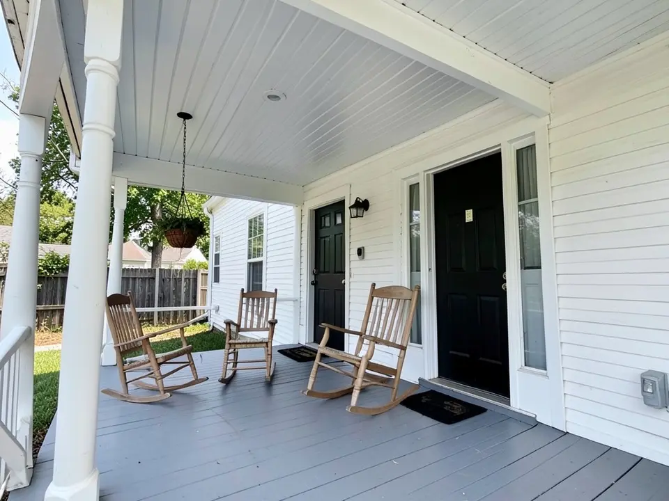 AI-drawn generic stand-in of a white farmhouse front porch seen from below, with a white plank ceiling, white posts, a gray painted floor, two rocking chairs, a black front door and a hanging plant