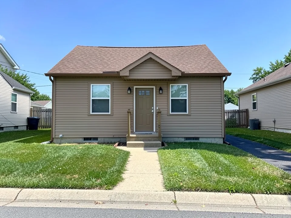 AI-drawn generic stand-in of a small single-story starter house with tan siding and trim, a small front stoop, a brown roof and a narrow driveway