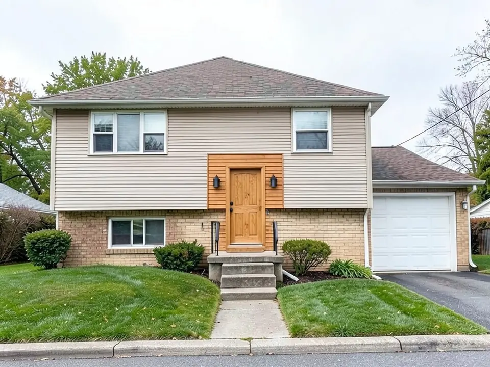 The same raised ranch with a natural wood front door, warm cedar boards on the wall around the door and a small black wall light on each side