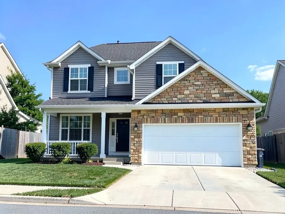 The same house with tan and brown stacked stone around and above the garage door and in the gable over the garage; gray siding kept on the rest